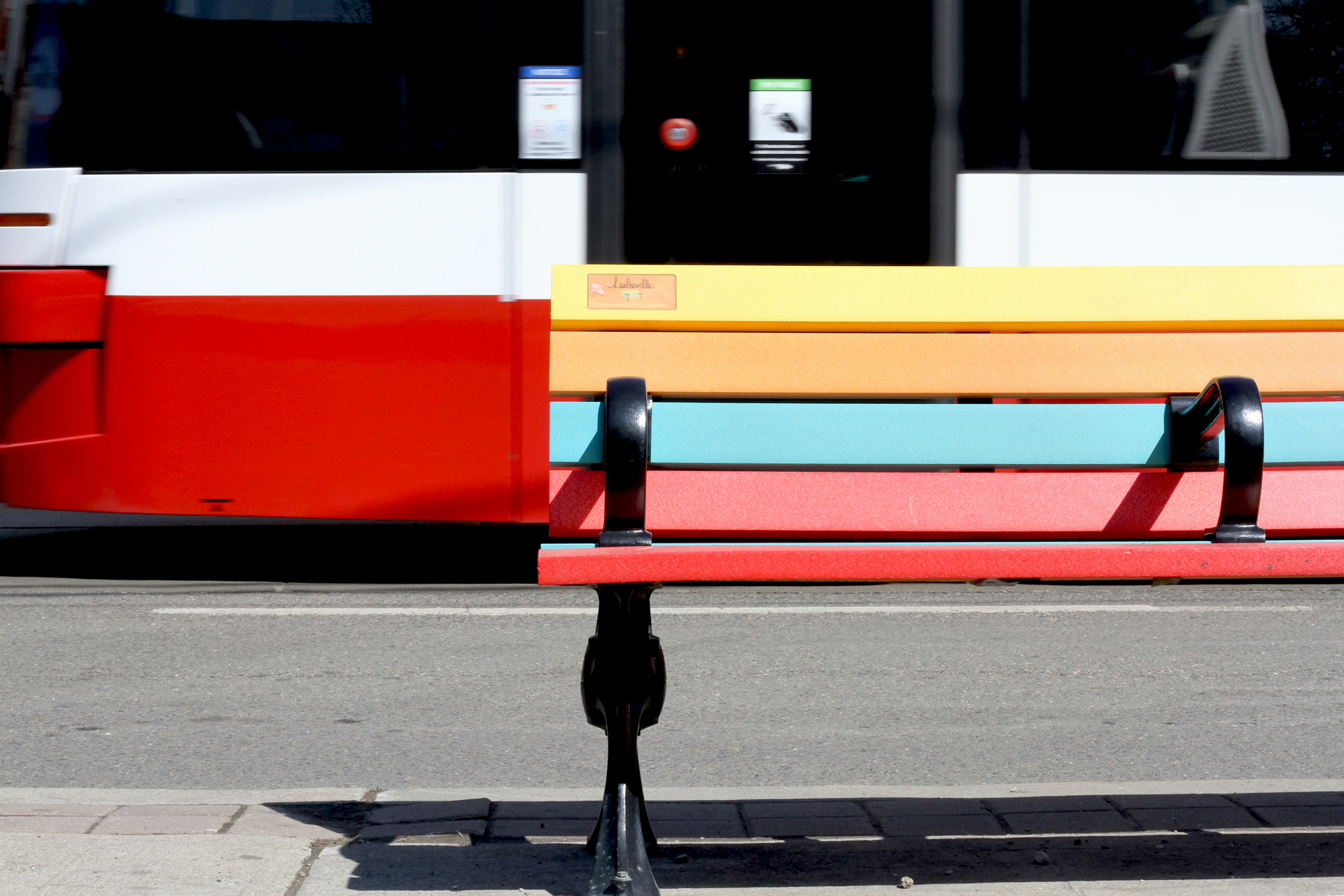 Iconic multicoloured Leslieville bench on Queen Street East with a passing TTC streetcar